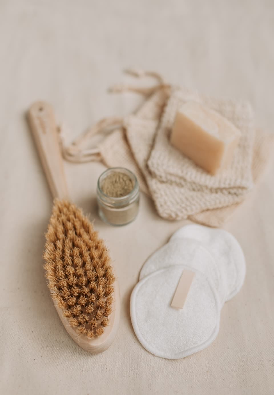 A bristle brush, reusable cotton pads and a bar of soap on linen