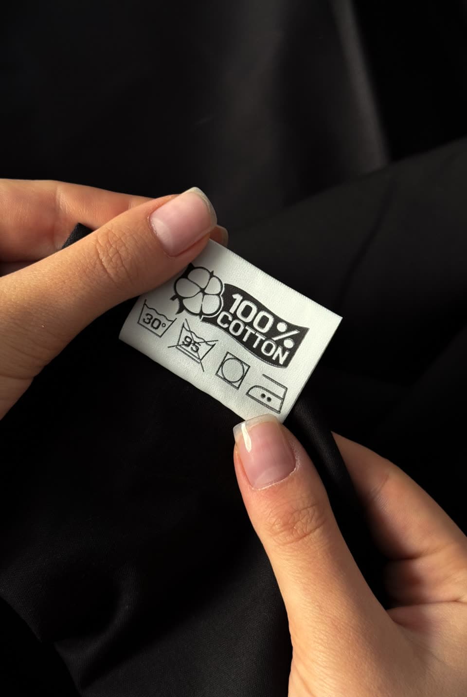 Fingers holding up a garment’s 100% cotton care label
