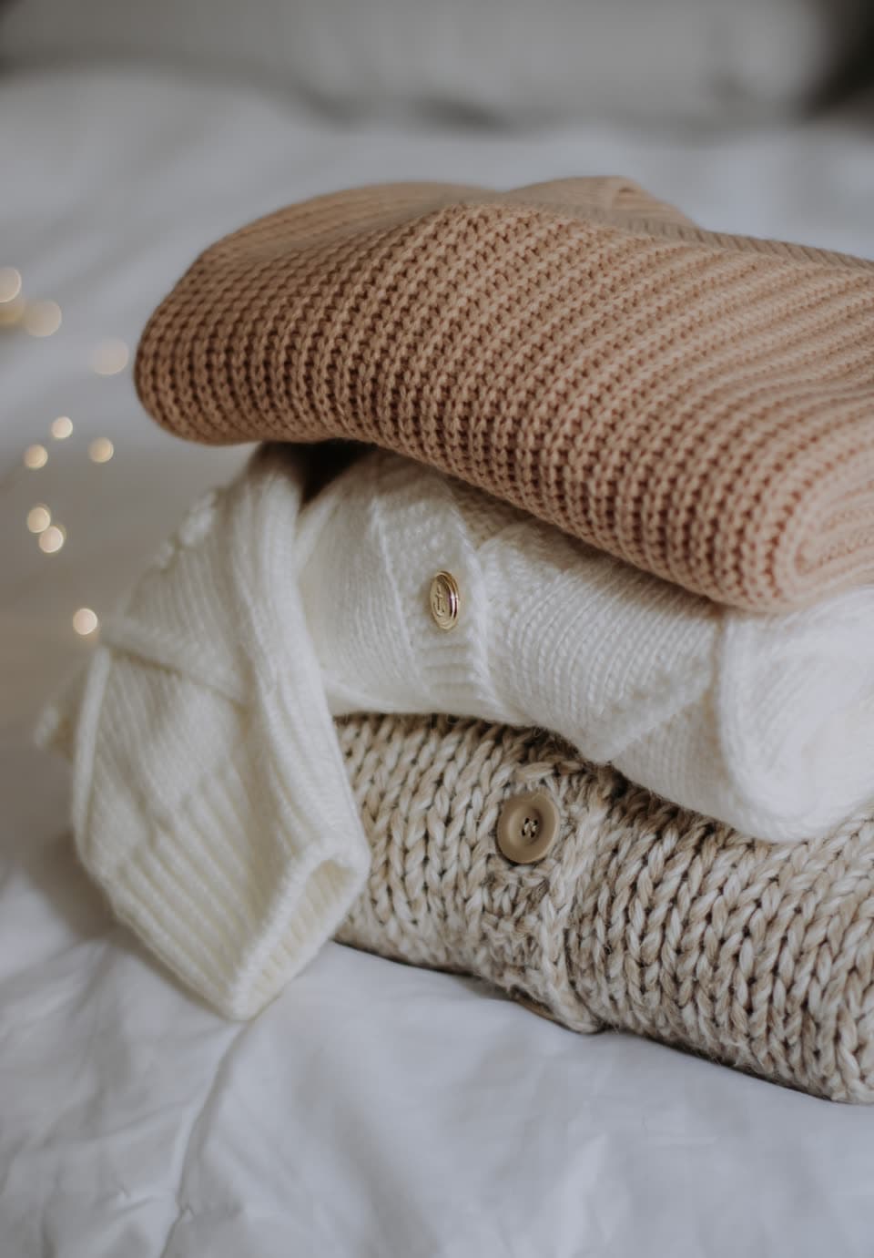 A stack of knitted jumpers and cardigans on a bed