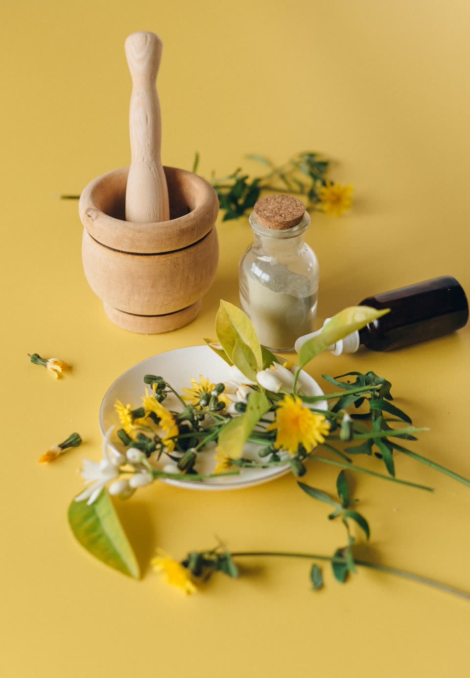 A wooden mortar and pestle, a cork-stoppered jar and fresh dandelions on yellow