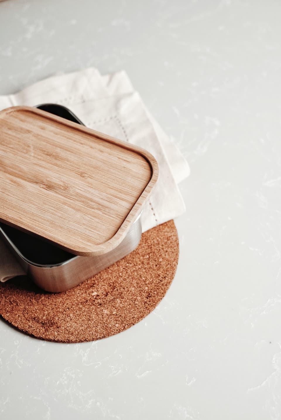 A steel lunchbox with a bamboo lid on a cork mat