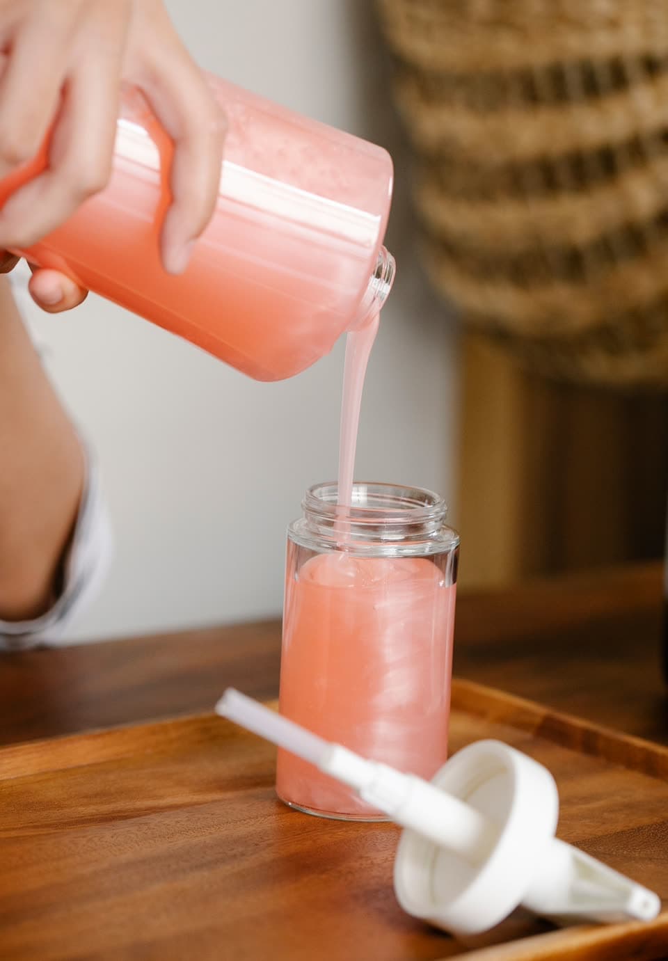 Pink soap poured from a refill jug into a glass pump bottle