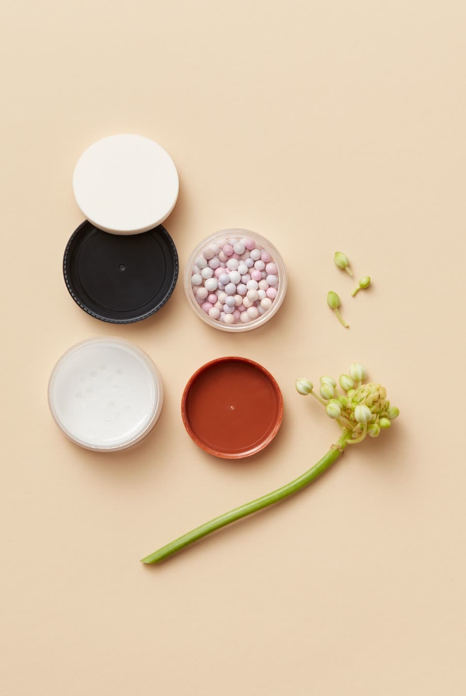 Open cosmetic pots with their lids off, laid out on a beige ground